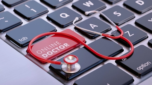 Red stethoscope draped over a laptop keyboard with a red key labelled Online Doctor highlighted at center