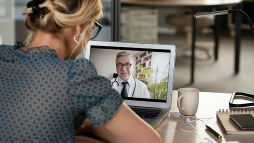 Person attends a telehealth consultation on a laptop with a doctor while seated at a desk